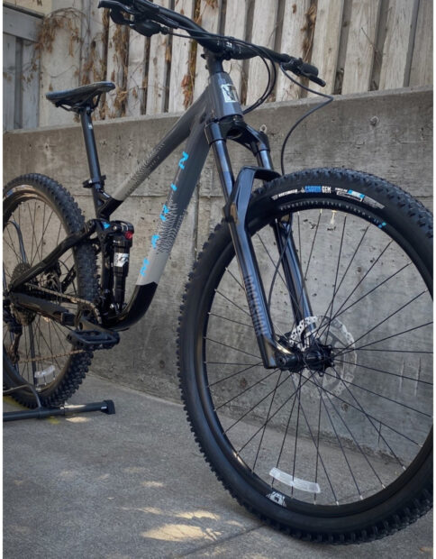 A gray Marin bike with thick tires stands on concrete near a faded wooden fence in sunlight, HD Mobile Wallpaper