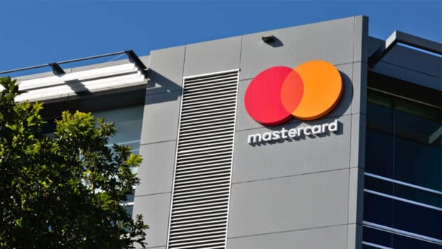 The Mastercard logo is displayed on a gray office building under a clear blue sky, 2K Desktop Wallpaper