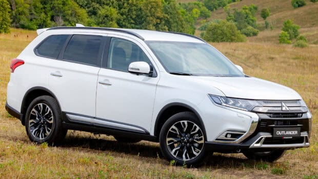 A white Mitsubishi Outlander is parked on a grassy field with trees in the background, HD Desktop Wallpaper