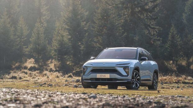 A Nio Auto Wallpapers ES6 car is parked on a grassy field surrounded by tall trees, HD Desktop Wallpaper