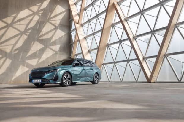 A teal Peugeot 308 is parked inside a bright building with geometric windows and wooden frames, 2K Desktop Wallpaper