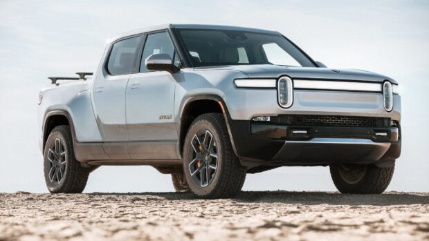 A silver Rivian truck stands on a sandy landscape under a clear sky with modern design features, HD Desktop Wallpaper