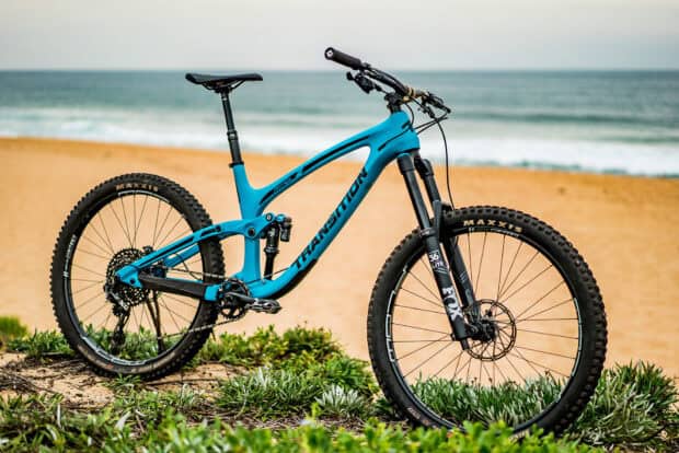 A modern blue Transition bike is parked on greenery near the sandy beach and ocean, HD Desktop Wallpaper