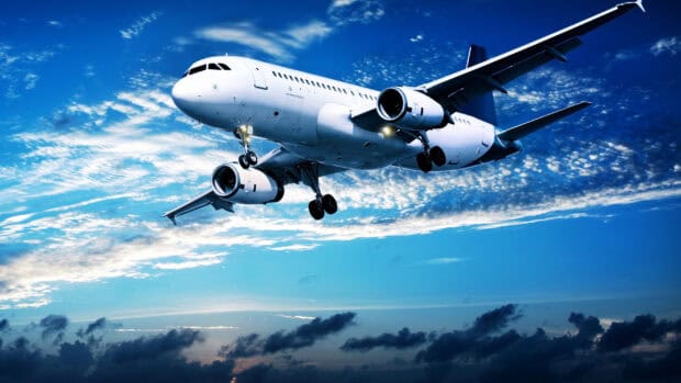 A modern commercial aircraft is flying above the clouds in a bright blue sky with scattered clouds, 2K Desktop Wallpaper