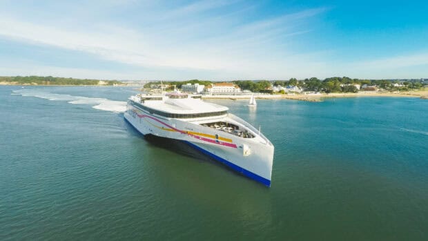 A modern ferry sails close to a coastal town under a bright sky, 4K Desktop Wallpaper