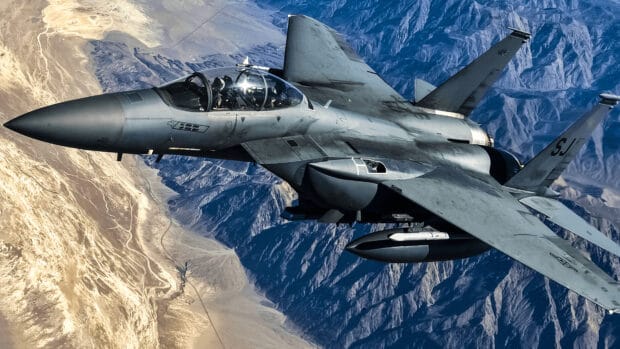 A jet fighter soars above rugged mountains with clear skies, 4K Desktop Wallpaper