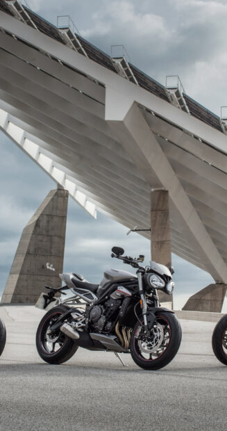 A sleek street bike is parked under a modern architectural structure on a cloudy day, 2K Mobile Wallpaper