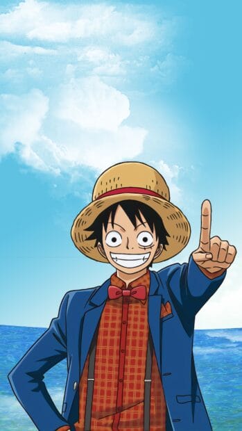 Monkey D Luffy is smiling and pointing upward by the ocean under a blue sky with clouds, 2K Phone Wallpaper