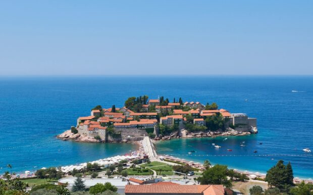 A scenic view of a coastal island with red rooftops and clear blue sea in Montenegro, 2K Desktop Wallpaper