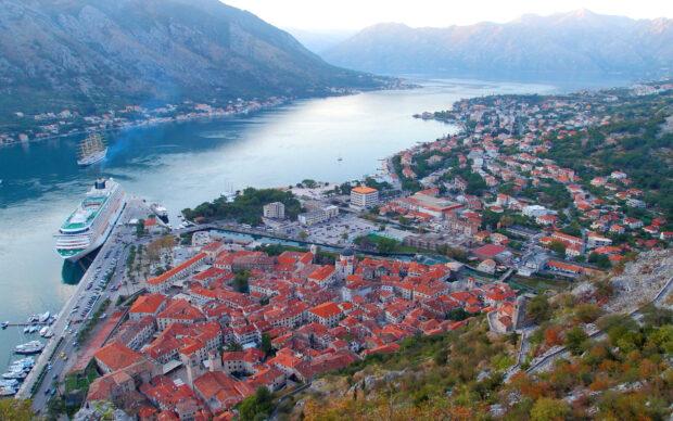 A scenic view of a Montenegro town by the water with red rooftops and surrounding mountains, 2K Desktop Wallpaper