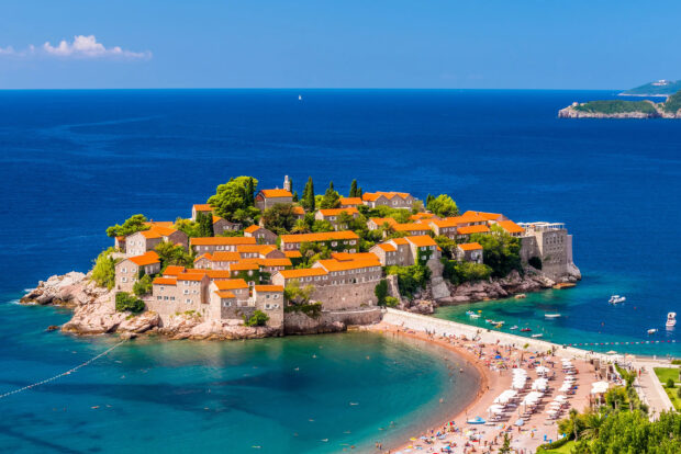 A scenic view of a Montenegro town with red roofs beside the clear blue sea and beach, 2K Desktop Wallpaper