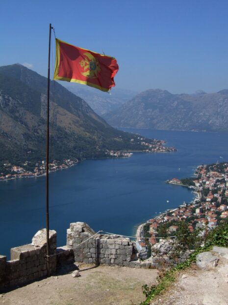 A red flag waves above the bay with mountains and villages in Montenegro featuring Montenegro wallpapers, 2K Desktop Wallpaper