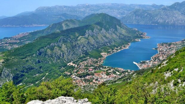 A panoramic view of Montenegro showing a bay surrounded by green mountains and a coastal town, HD Desktop Wallpaper