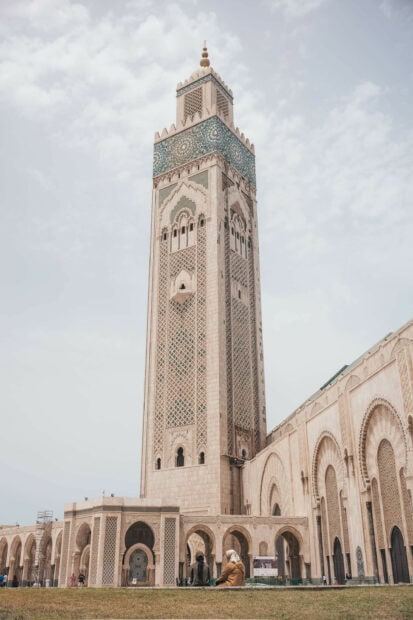 The Moroccan tower stands tall with detailed patterns and people sitting nearby, 2K Desktop Wallpaper
