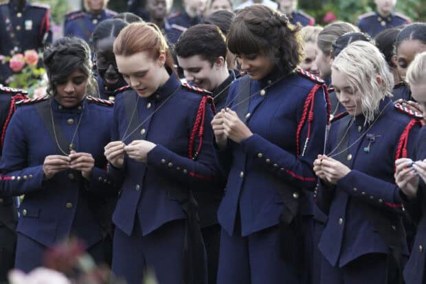 The cast of Motherland Fort Salem is shown wearing military uniforms while holding necklaces in a solemn moment, 2K Desktop Wallpaper
