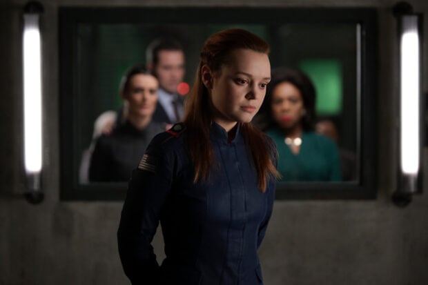 A woman in a military uniform is in focus with three blurred people behind her in a dimly lit room, 2K Desktop Wallpaper