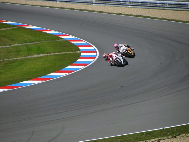 Two motorcyclists are racing closely on a curved race track during a sunny day, HD Desktop Wallpaper