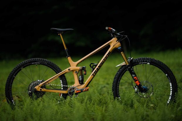 A mountain bike from Transition Bikes is shown resting in a grassy field with detailed suspension and tires, 2K Desktop Wallpaper