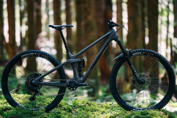 A sleek matte black mountain bike stands in a lush forest setting showcasing Transition Bikes Wallpapers, 2K Desktop Wallpaper