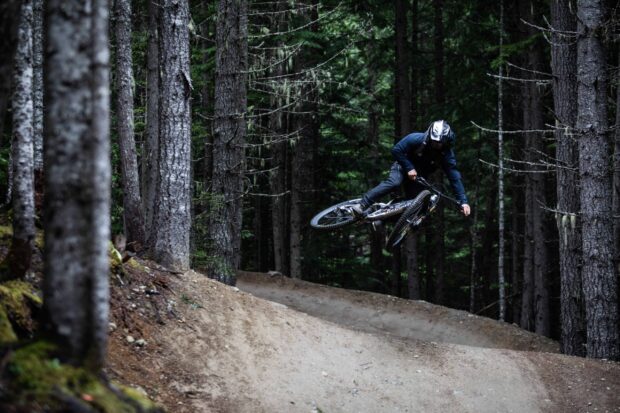 A mountain biker rides over a dirt trail while jumping in the forest, 2K Desktop Wallpaper