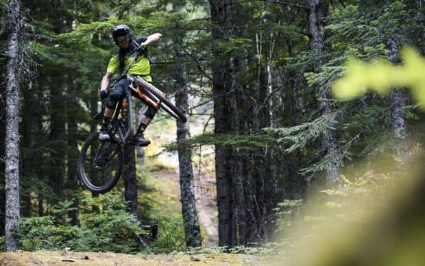 A mountain biker rides a Transition bike through a forest trail showing intense action and skill, HD Desktop Wallpaper