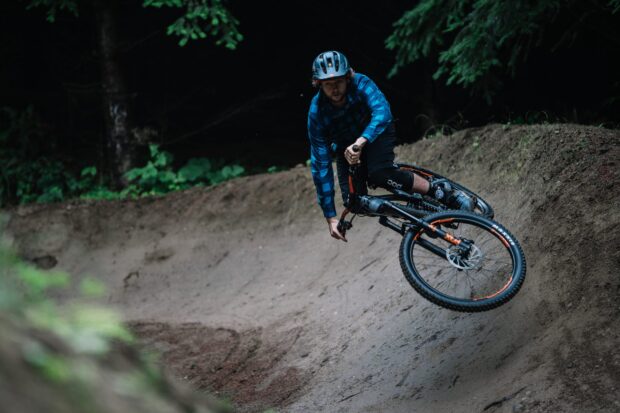 A man wearing a helmet rides a transition bike on a curved dirt track in the forest, 2K Desktop Wallpaper