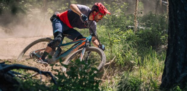 A man wearing protective gear rides a Bmc bike through a dusty forest trail, 2K Desktop Wallpaper