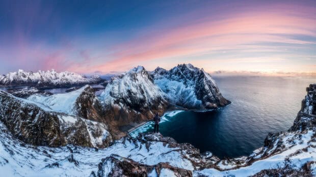 A person stands overlooking snow covered mountains and glacier waters at sunset, 4K Desktop Wallpaper