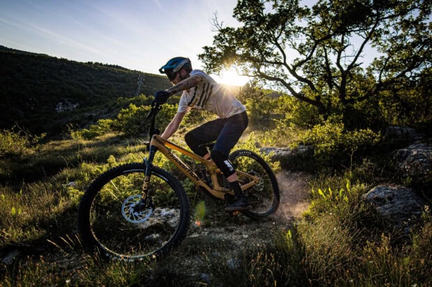 A man rides a Transition bike on a rugged mountain trail under the bright sun, 2K Desktop Wallpaper