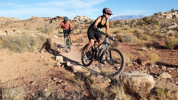 Two cyclists riding Marin bikes on a rocky desert trail with mountains in the background, 2K Desktop Wallpaper