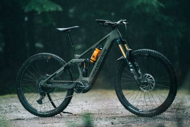 A mountain trail bike with the Transition Bikes logo is standing in the rain on a forest path, 2K Desktop Wallpaper