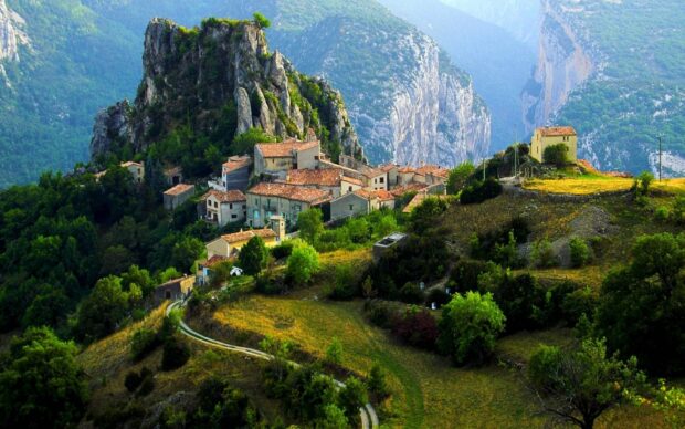 A mountain village is surrounded by lush green hills and rocky cliffs in the distance, HD Desktop Wallpaper