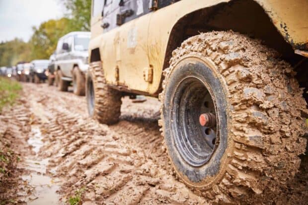 Mud covered tires on off road vehicles driving through a muddy trail in a forest, 2K Desktop Wallpaper
