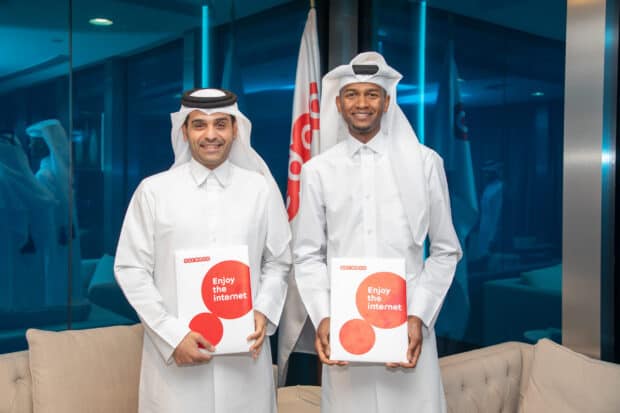 Mutaz Essa Barshim is smiling and holding Ooredoo packages in a modern office, 2K Desktop Wallpaper