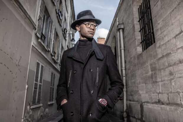 Mutaz Essa Barshim stands confidently in a dark coat and hat on a city street, HD Desktop Wallpaper