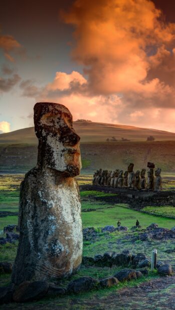 A large Easter Island statue stands in a grassy field with other statues and a colorful sunset sky, HD Mobile Wallpaper