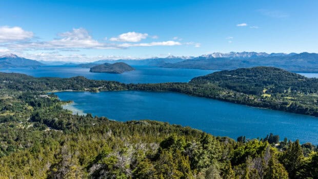 The breathtaking Nahuel Huapi landscape shows blue waters surrounded by forested hills and distant snowy mountains, 4K Desktop Wallpaper