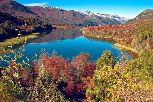 The Nahuel Huapi lake reflects autumn trees and surrounding mountains under a clear blue sky, 2K Desktop Wallpaper