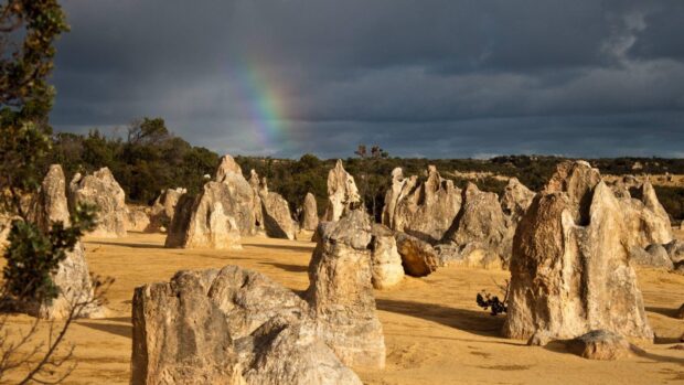 A vibrant landscape of Nambung National Park rock formations under a cloudy sky with a rainbow, HD Desktop Wallpaper