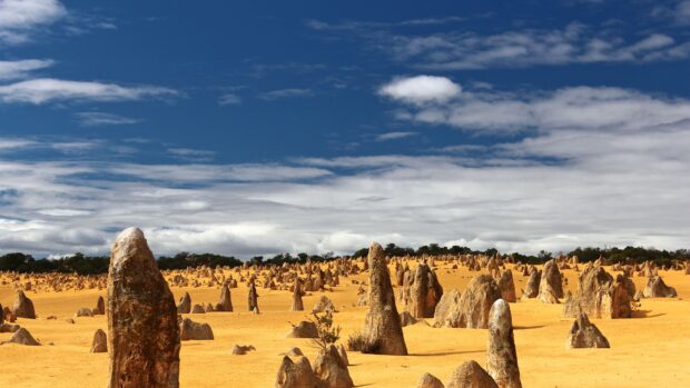 Tall limestone formations rising from yellow sand under a blue sky at Nambung National Park, 4K Desktop Wallpaper