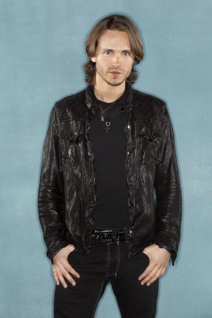 A man wearing a black leather jacket stands against a blue background from Nashville TV series, 2K Mobile Wallpaper