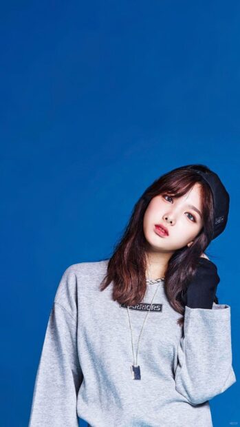 A woman wearing a grey sweatshirt and black cap looks at the camera with a blue background in Nayeon wallpapers, HD Mobile Wallpaper