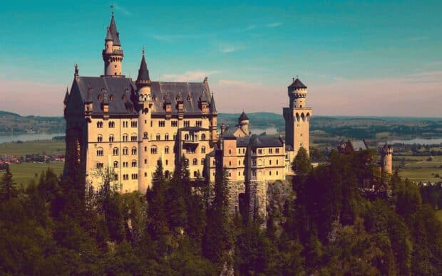 Neuschwanstein Castle surrounded by forest under a clear blue sky, 2K Desktop Wallpaper
