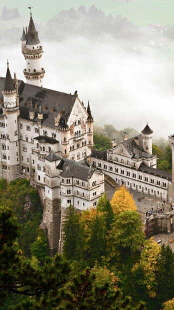 A stunning view of Neuschwanstein Castle surrounded by autumn trees and mist, 4K Phone Wallpaper