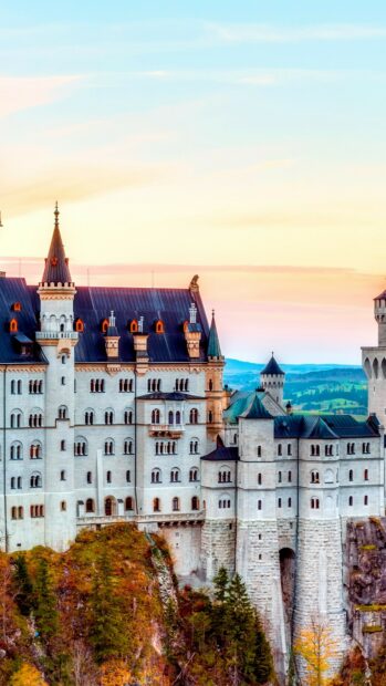 Neuschwanstein Castle stands tall over autumn trees with a sunset sky, 4K Phone Wallpaper