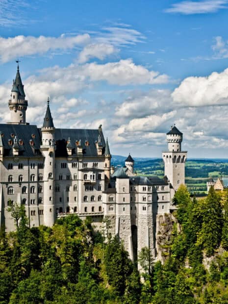 Neuschwanstein Castle stands majestically amid green forests and blue skies, 2K Desktop Wallpaper