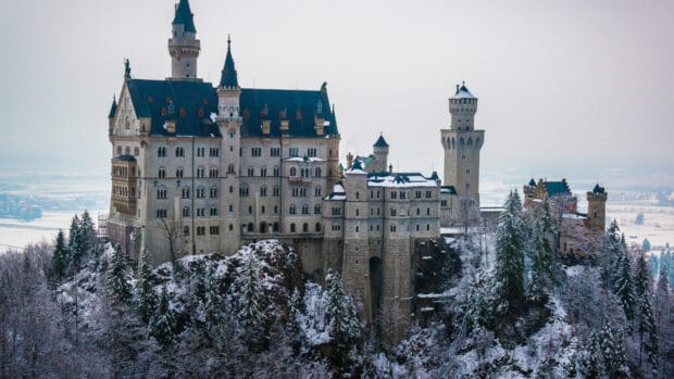 Neuschwanstein Castle surrounded by snow covered trees and rocky cliffs in winter, 4K Desktop Wallpaper