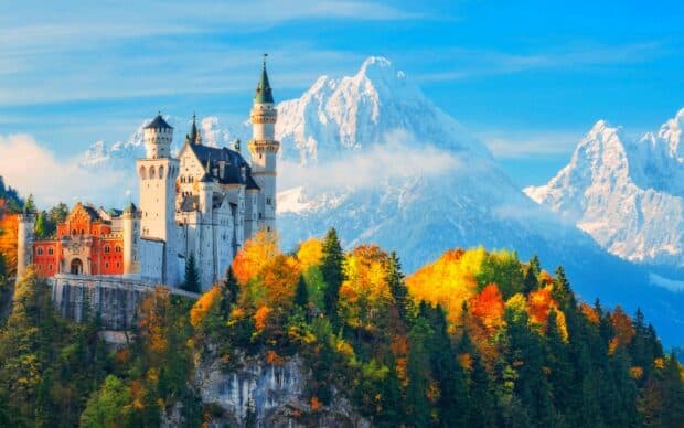 Neuschwanstein Castle surrounded by vibrant autumn trees and snowy mountains, HD Desktop Wallpaper