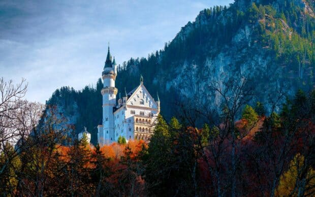 Neuschwanstein Castle stands surrounded by colorful autumn trees and a mountain backdrop, HD Desktop Wallpaper