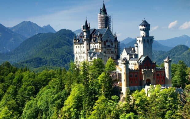 A scenic view of Neuschwanstein Castle surrounded by dense forest and mountains, 2K Desktop Wallpaper